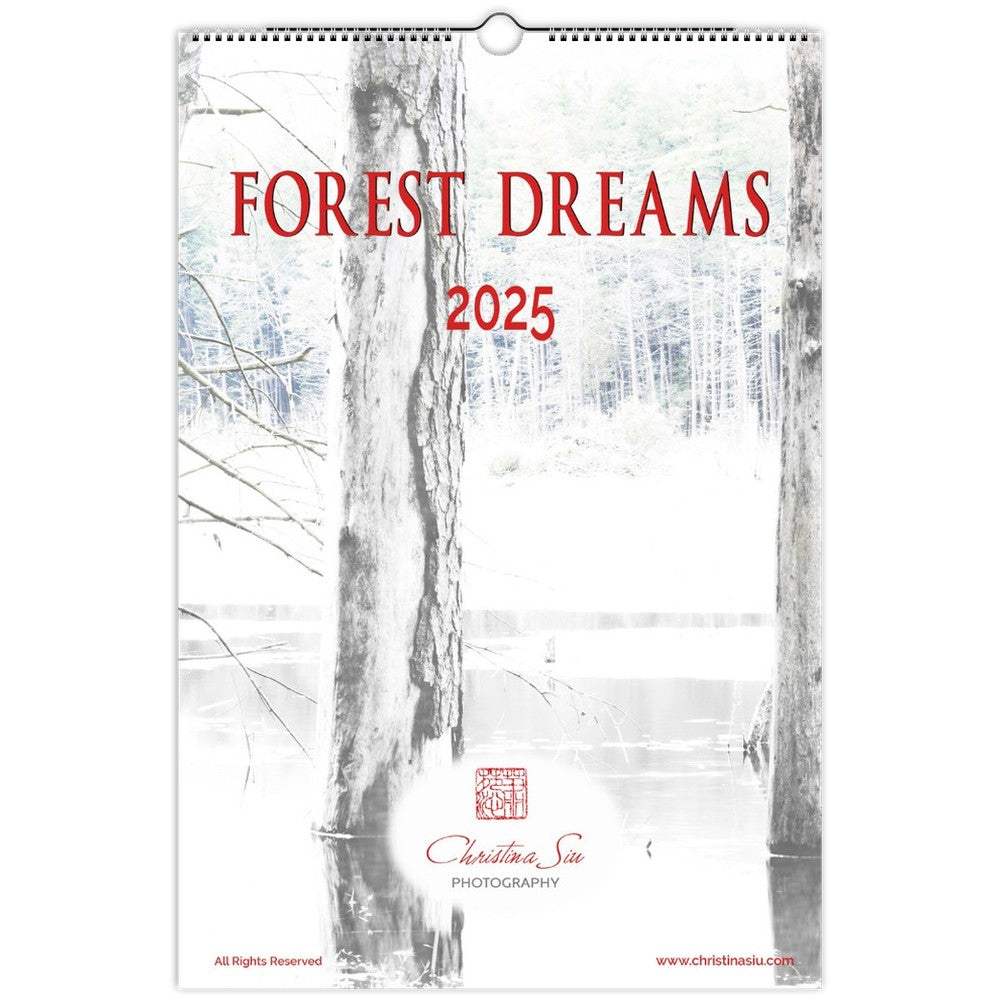 Forest Dreams ledger wall calendar showing a snippet of a forest of trees and water in the background and tree trunks in the foreground. The color is a desaturated pastel white/grey color with font in a crimson red.